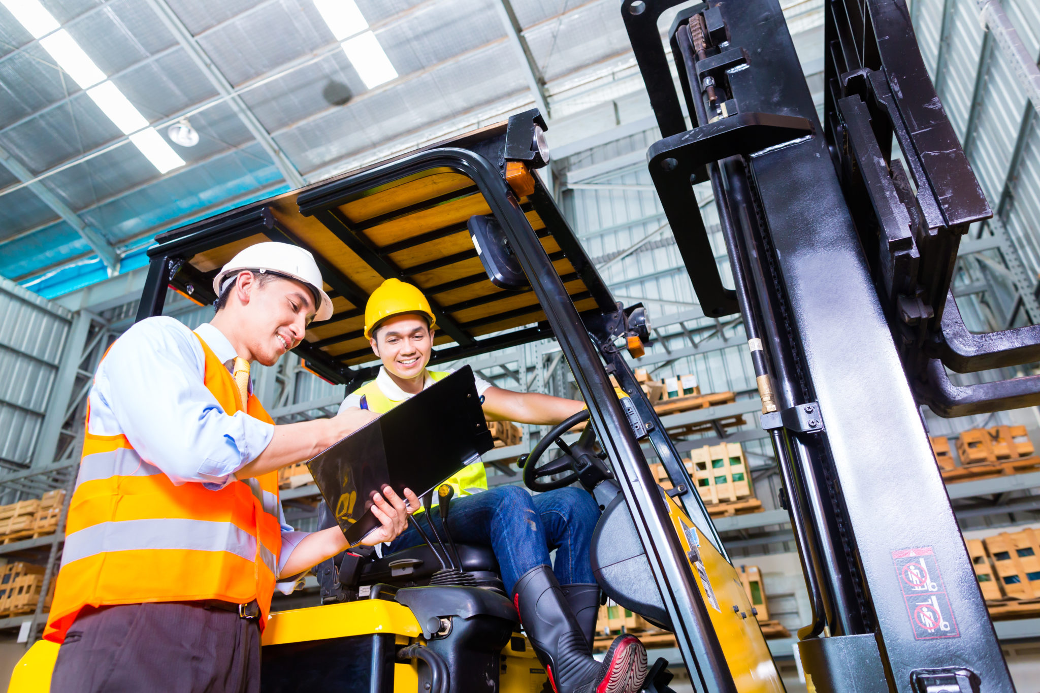 Asian fork lift truck driver discussing checklist with foreman in warehouse