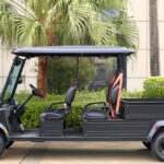 Left side view of the medium bed, four-seater, black Fusion commercial utility vehicle parked near shrubbery and trees.