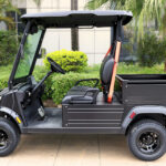 Left side view of the short bed, two-seater, black Fusion commercial utility vehicle parked near shrubbery and trees.